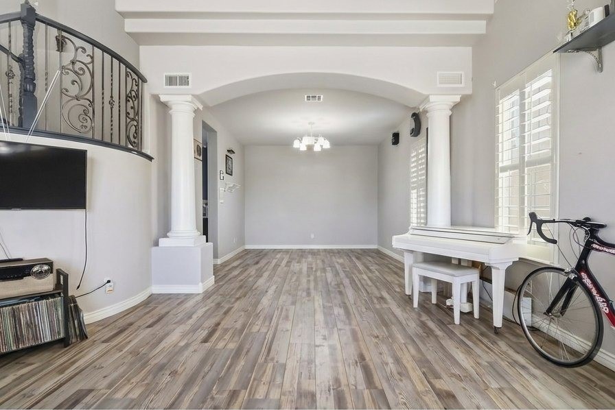 Formal living and dining area at 9564 Trattoria Street with iron staircase, wide-plank floors, and white grand piano